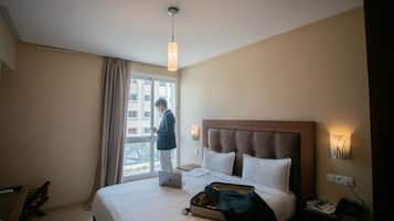 Una habitación de hotel con cama, escritorio, computadora portátil, maleta y ventana con cortinas.