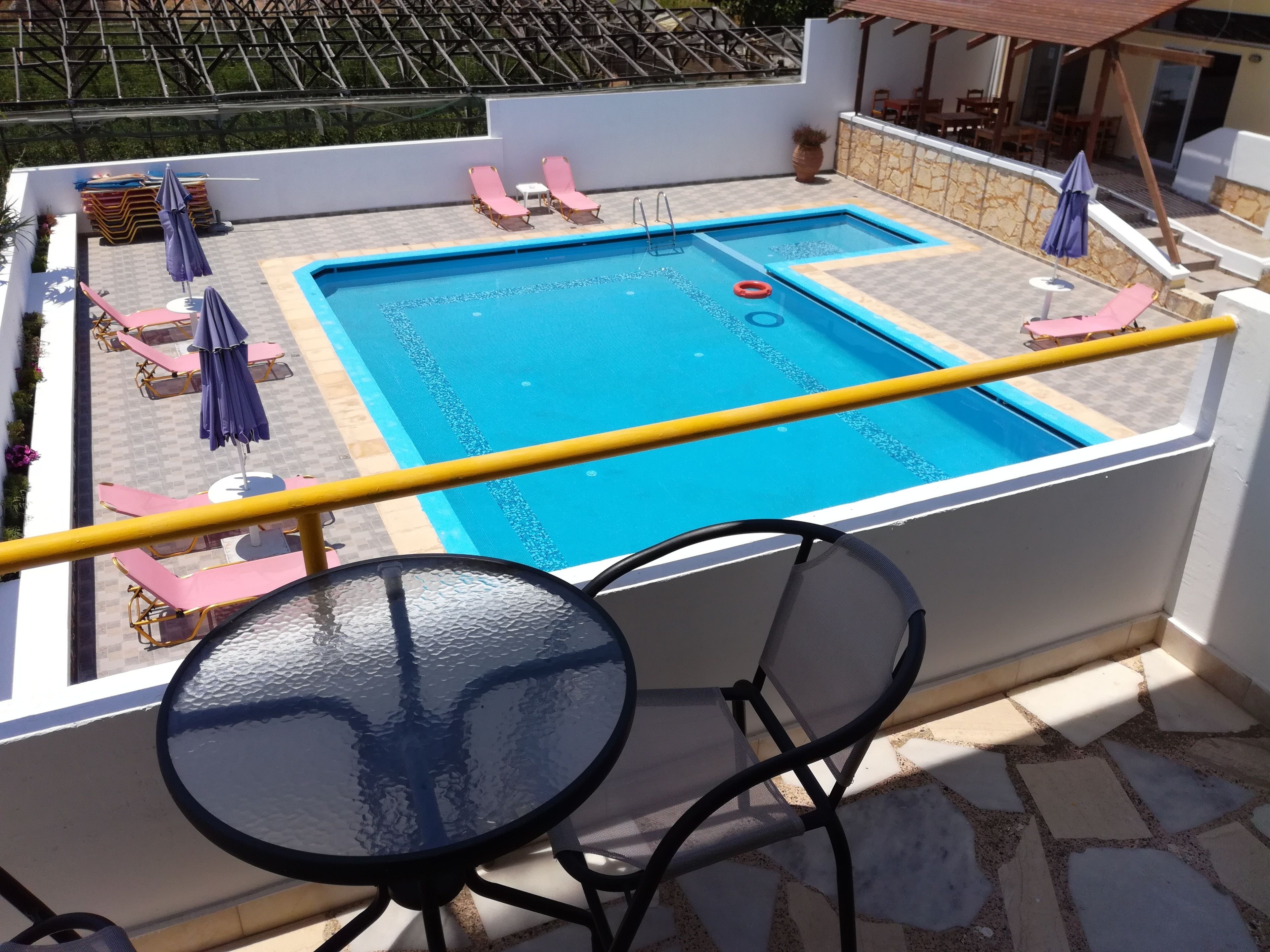 Ein Poolbereich auf dem Dach mit Glastisch und -stühlen, Liegestühlen und Sonnenschirmen.