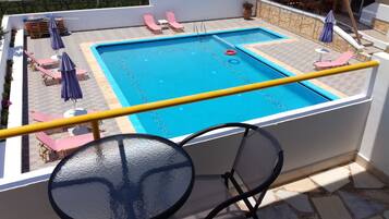 Ein Poolbereich auf dem Dach mit Glastisch und -stühlen, Liegestühlen und Sonnenschirmen.