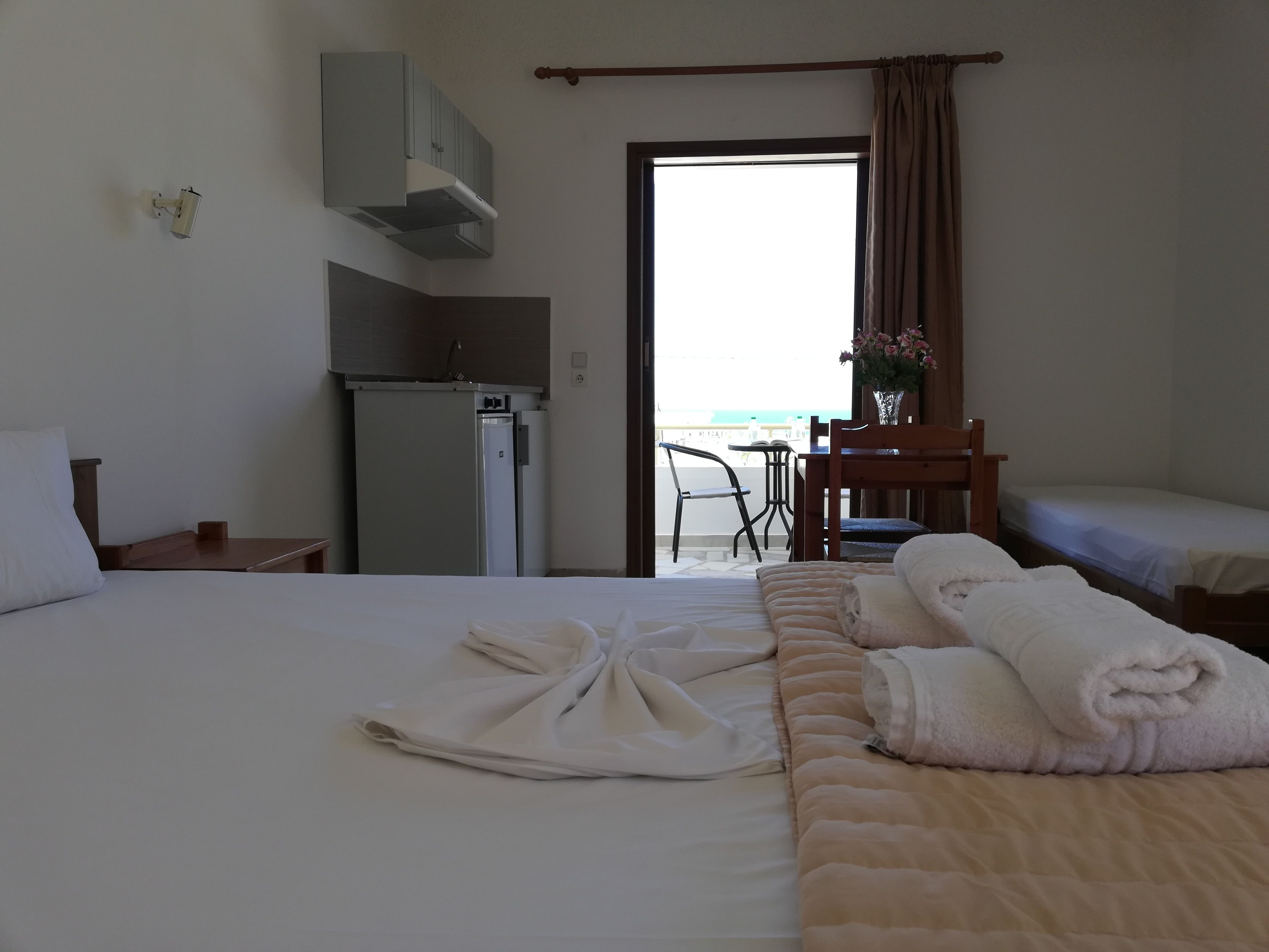 Ein Hotelzimmer mit Bett, Schreibtisch, Kühlschrank, Stuhl und Blick auf den Strand.