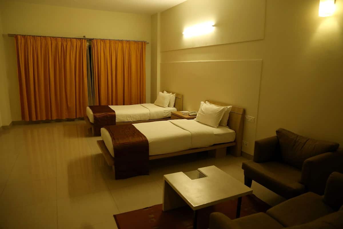 A hotel room with two beds, a sofa, a small table, and a curtain.