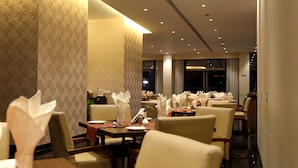 A well-lit dining area with tables set for service, featuring patterned wallpaper and modern decor. - Hotel EEFA (Belagavi)