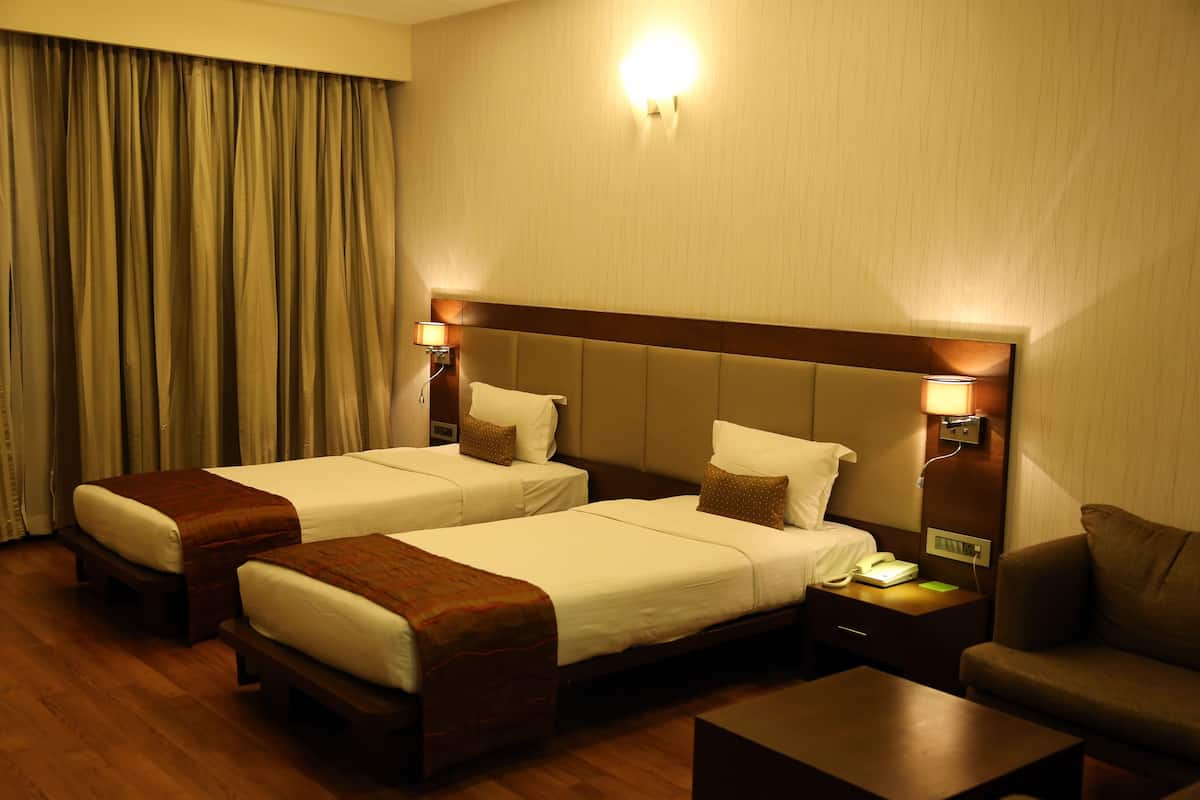 A hotel room with two beds, a sofa, a coffee table, and a nightstand with a lamp.