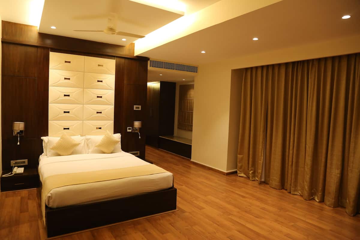 A modern hotel room with a large bed, wooden flooring, a built-in headboard, and a large window with curtains.