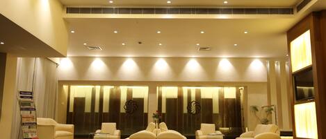A modern lobby with a reception desk, seating area, and a large window with blinds.