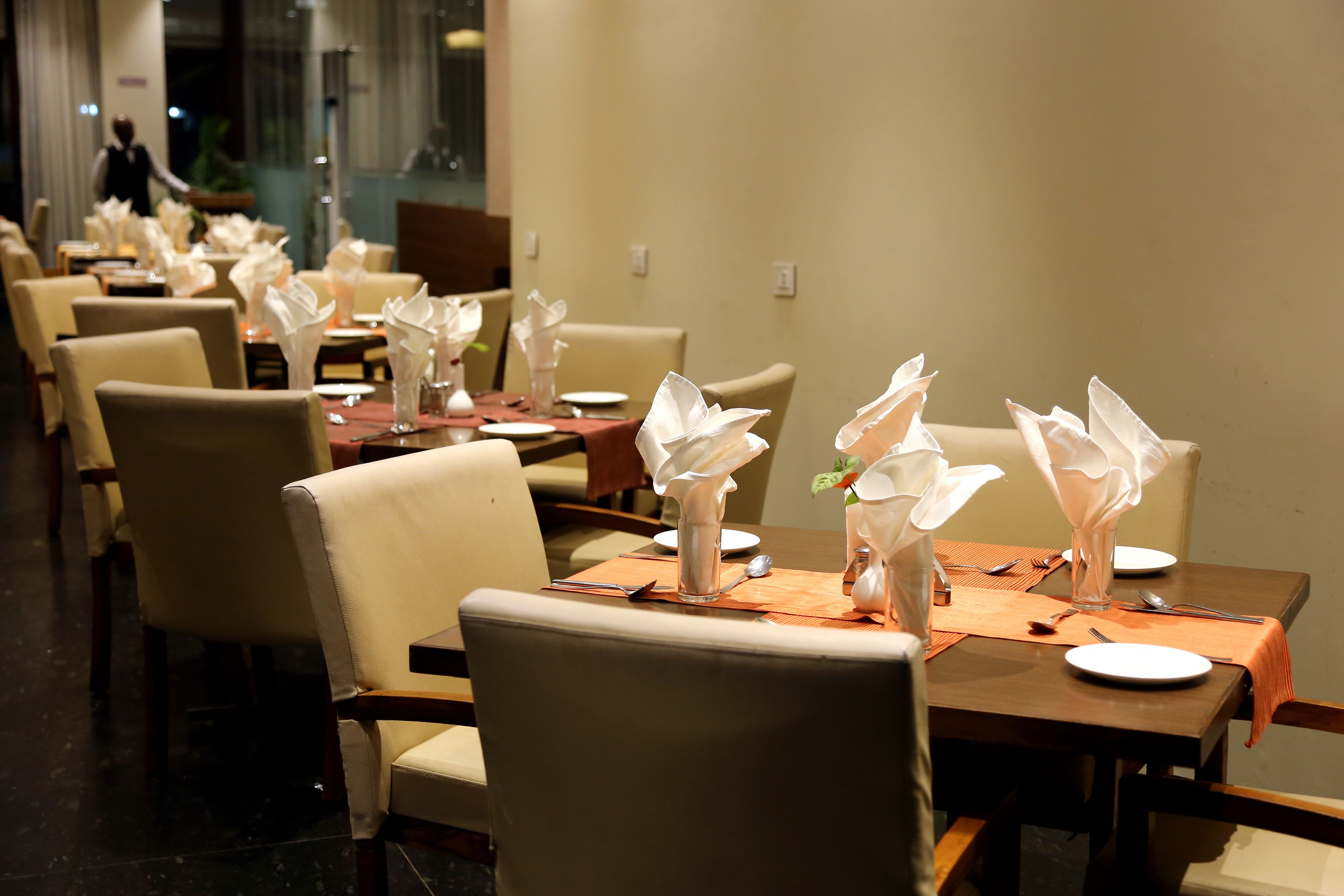 Een restaurant met meerdere tafels, gedekt met witte servetten, borden en bestek.