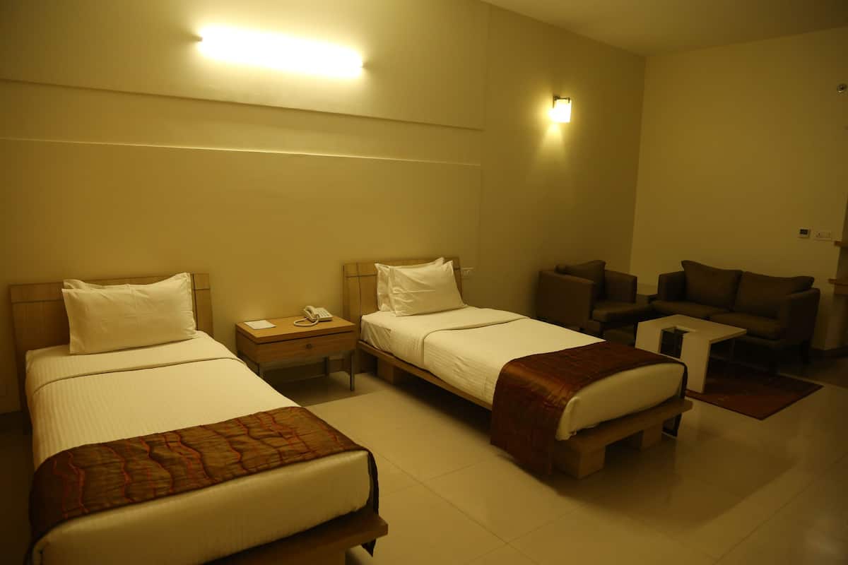 A hotel room with two single beds, a small sofa, a nightstand with a phone, and a wall-mounted light.