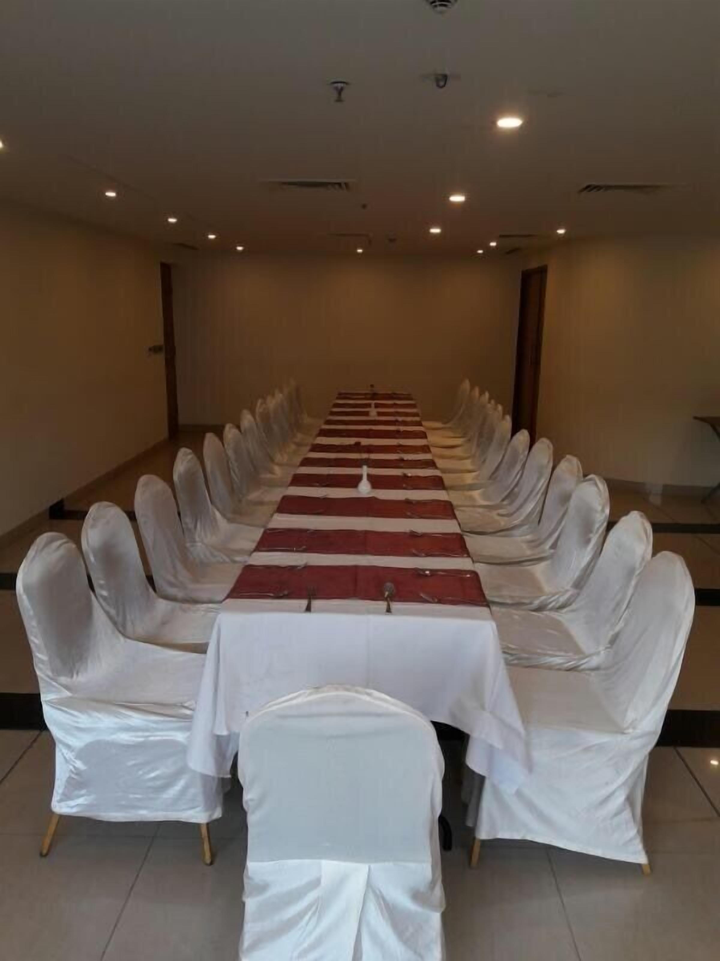 A conference room with a long table, white chairs, and a red and white table runner.