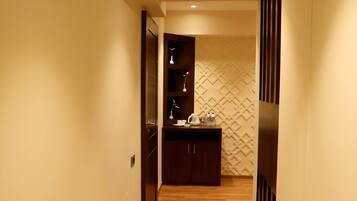 A narrow hallway with wooden flooring leading to a kitchen area with dark cabinets and a patterned backsplash.