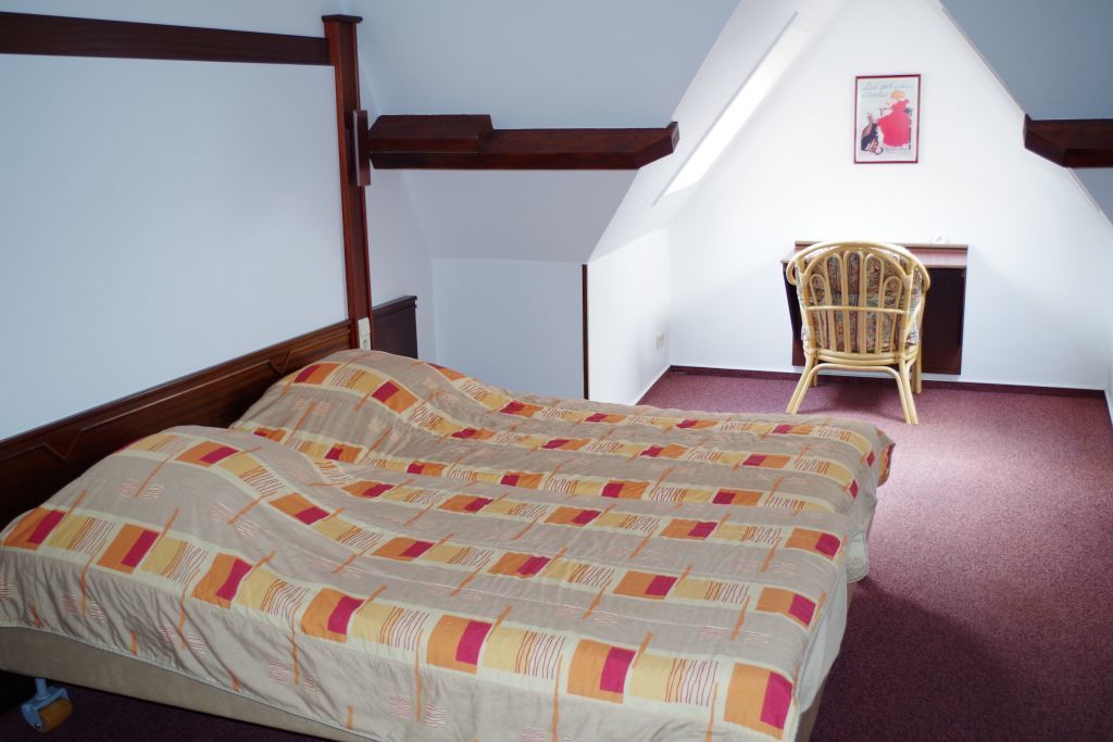 A bedroom with a bed, a chair, and a sloped ceiling.