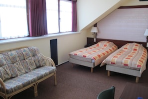 A room with two single beds, a sofa, a window with curtains, and a lamp. - Vakantiecentrum Zeelinde (De Haan)