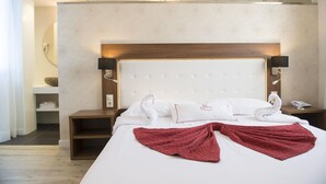 Una habitación de hotel con una cama grande, un cabecero de madera, dos lámparas de noche y una mesita de noche con un teléfono y un cuenco.