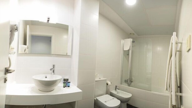 A modern bathroom with a white sink, mirror, and toilet. It includes a shower area with a glass door and a towel rack. - Hotel El Mudayyan (Teruel)