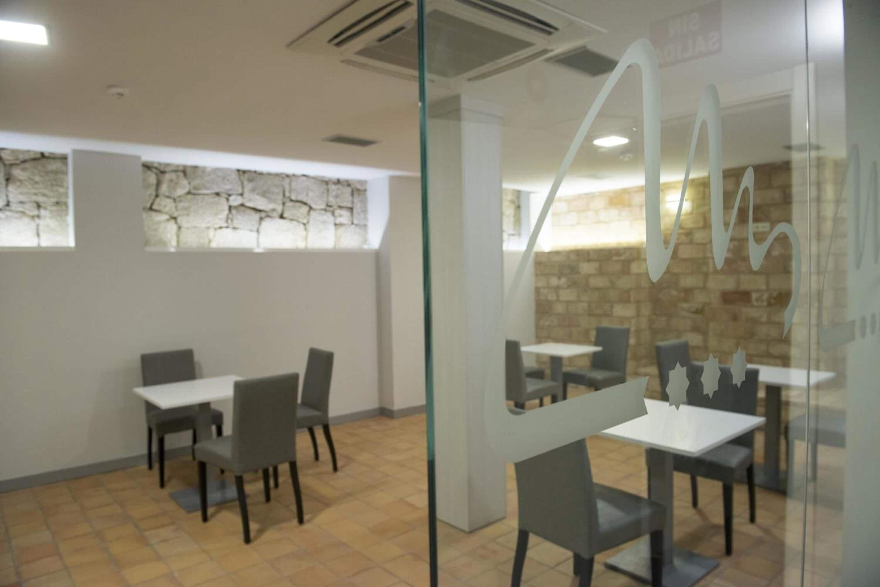 Un restaurante con mesas y sillas, paredes de piedra y una partición de vidrio.