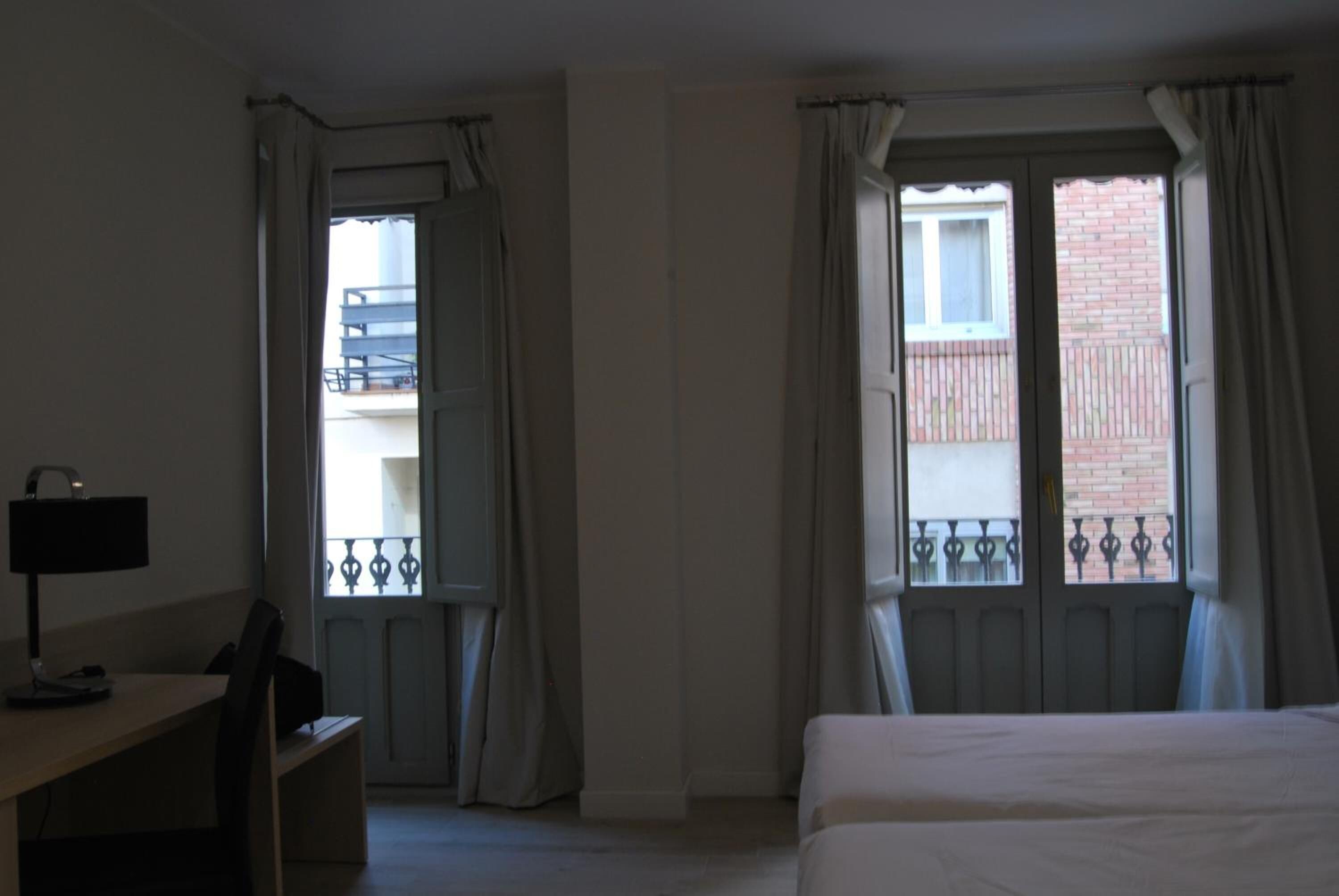 Una habitación de hotel con una cama, un escritorio y dos ventanas con cortinas.