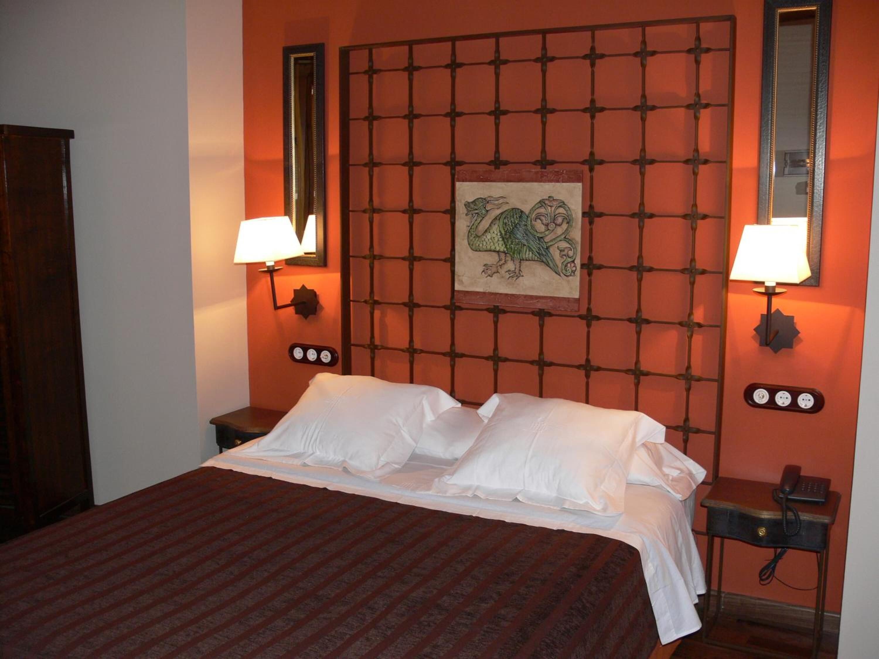 A hotel room with a bed, two bedside tables, a nightstand, a wall-mounted lamp, a mirror, and a decorative panel with a dragon design.