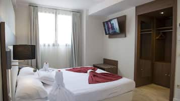 A hotel room with a bed, a television mounted on the wall, a wardrobe, and a window with curtains.