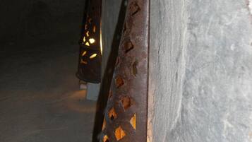 Primer plano de un farol rústico de metal con un diseño de corte de rombos, fijado en una pared de piedra.