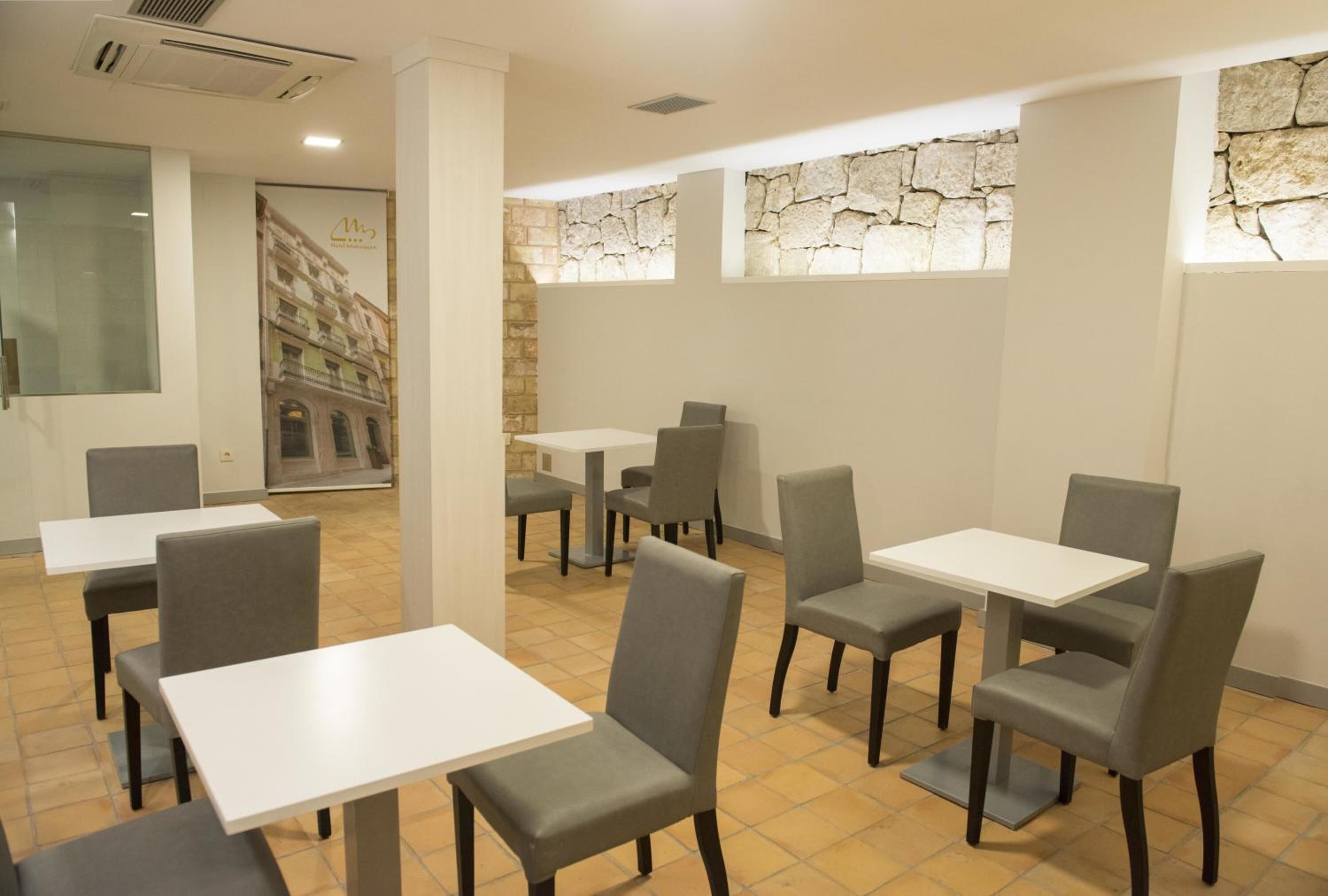 A restaurant with white tables and grey chairs, stone walls, and a tiled floor.