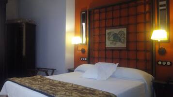 A hotel room with a large bed, two bedside lamps, a wall-mounted clock, and a framed picture above the bed.