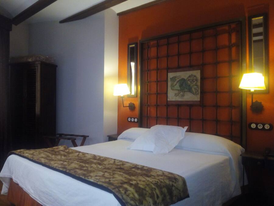 A hotel room with a large bed, two bedside lamps, a wall-mounted clock, and a framed picture above the bed.