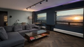 A modern living room with a sofa, a glass coffee table, and a view of the sunset through large windows. - The Penthouse (The Hague)