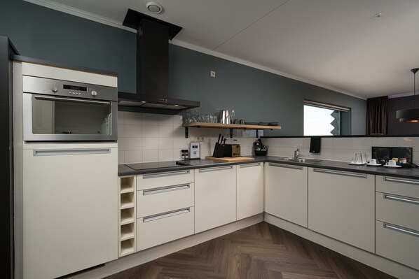 A modern kitchen with white cabinets, a built-in oven, and a black range hood. - The Penthouse (The Hague)