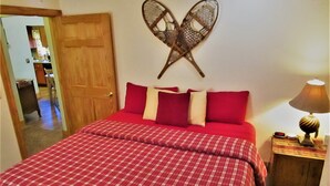 Una cama con colcha escocesa roja, una puerta de madera y un adorno colgado en la pared.