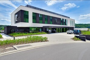 A modern hotel building with a flat roof, large windows, and a parking area.