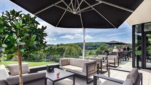 An outdoor patio area with a large umbrella, sofas, and tables. - R hotel experiences (Aywaille)