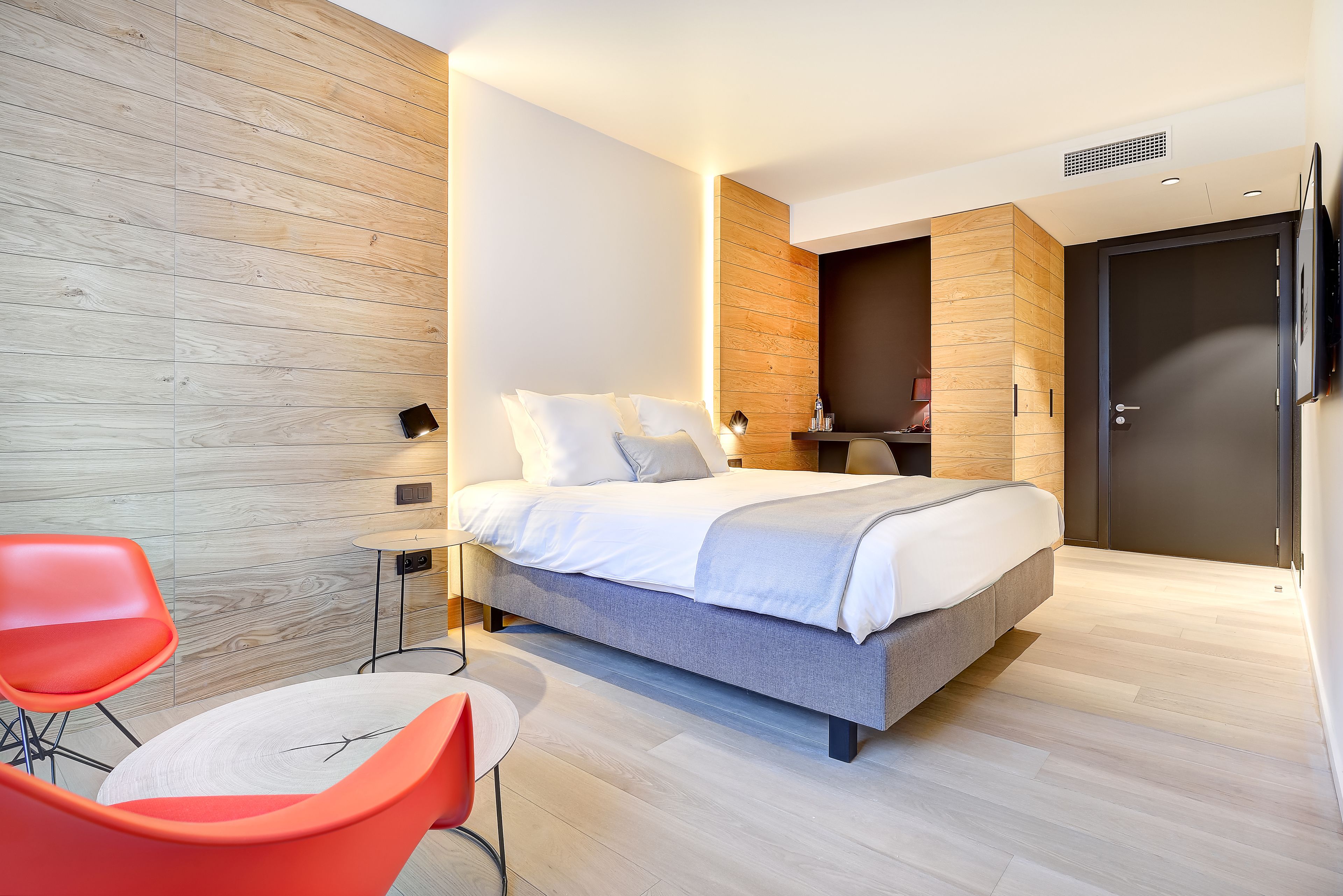 Een moderne slaapkamer met een bed, twee stoelen, een nachtkastje en een kledingkast.