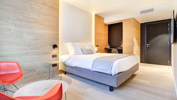 Een moderne slaapkamer met een bed, twee stoelen, een nachtkastje en een kledingkast.