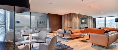 A modern living room with a glass table, patterned chairs, a leather sofa, and a large window with blinds.