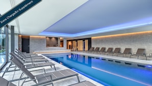 A modern indoor swimming pool with lounge chairs and a stone wall. - R hotel experiences (Aywaille)