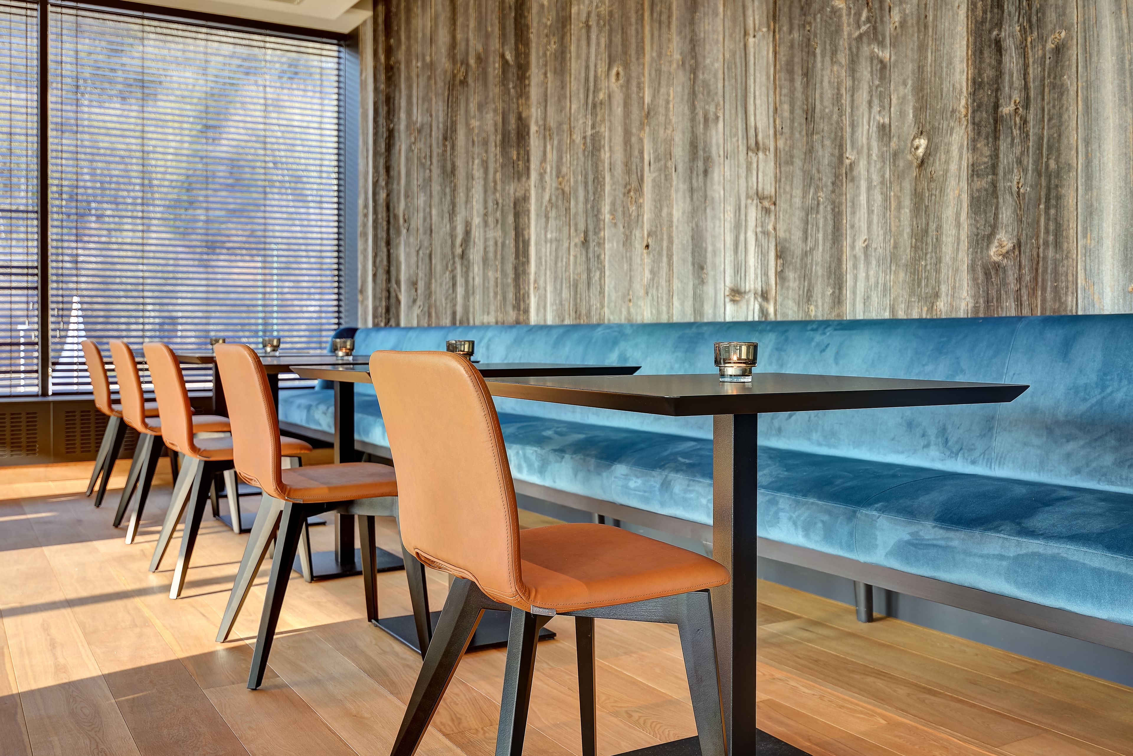 Interior moderno de restaurante con suelo de madera, un banco acolchado azul y sillas naranja.