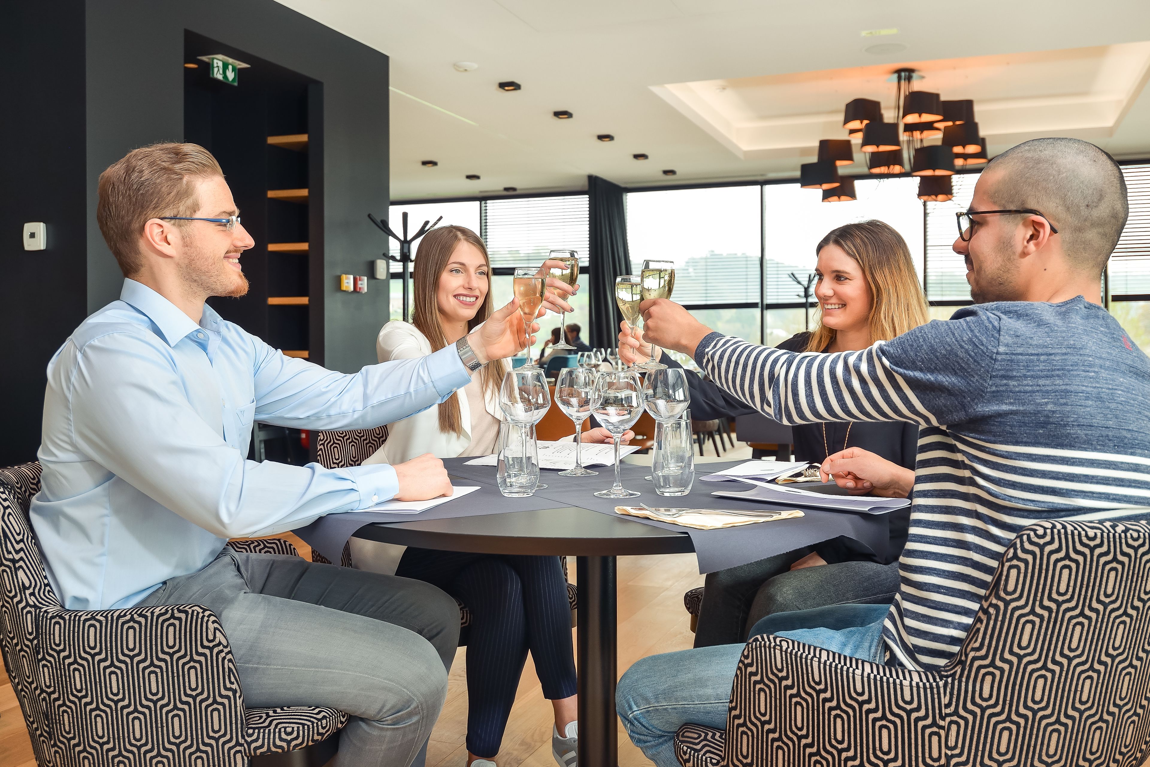 Un groupe de personnes porte un toast autour d’une table dans un espace intérieur moderne, avec vue sur les bâtiments à l’extérieur.