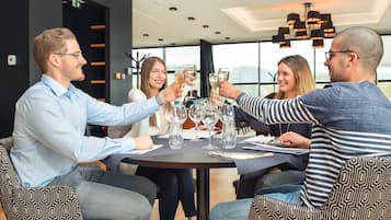 Un groupe de personnes porte un toast autour d’une table dans un espace intérieur moderne, avec vue sur les bâtiments à l’extérieur.