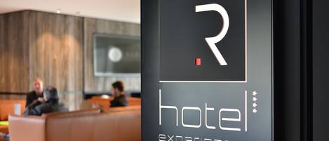 Un hall d’accueil moderne, avec un grand logo en forme de « R » et les mots « expériences hôtelières » inscrits sur le mur.