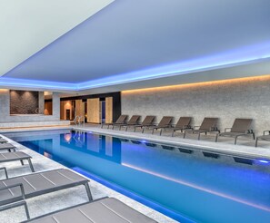 Una piscina interior moderna con sillones de descanso y una pared de piedra.