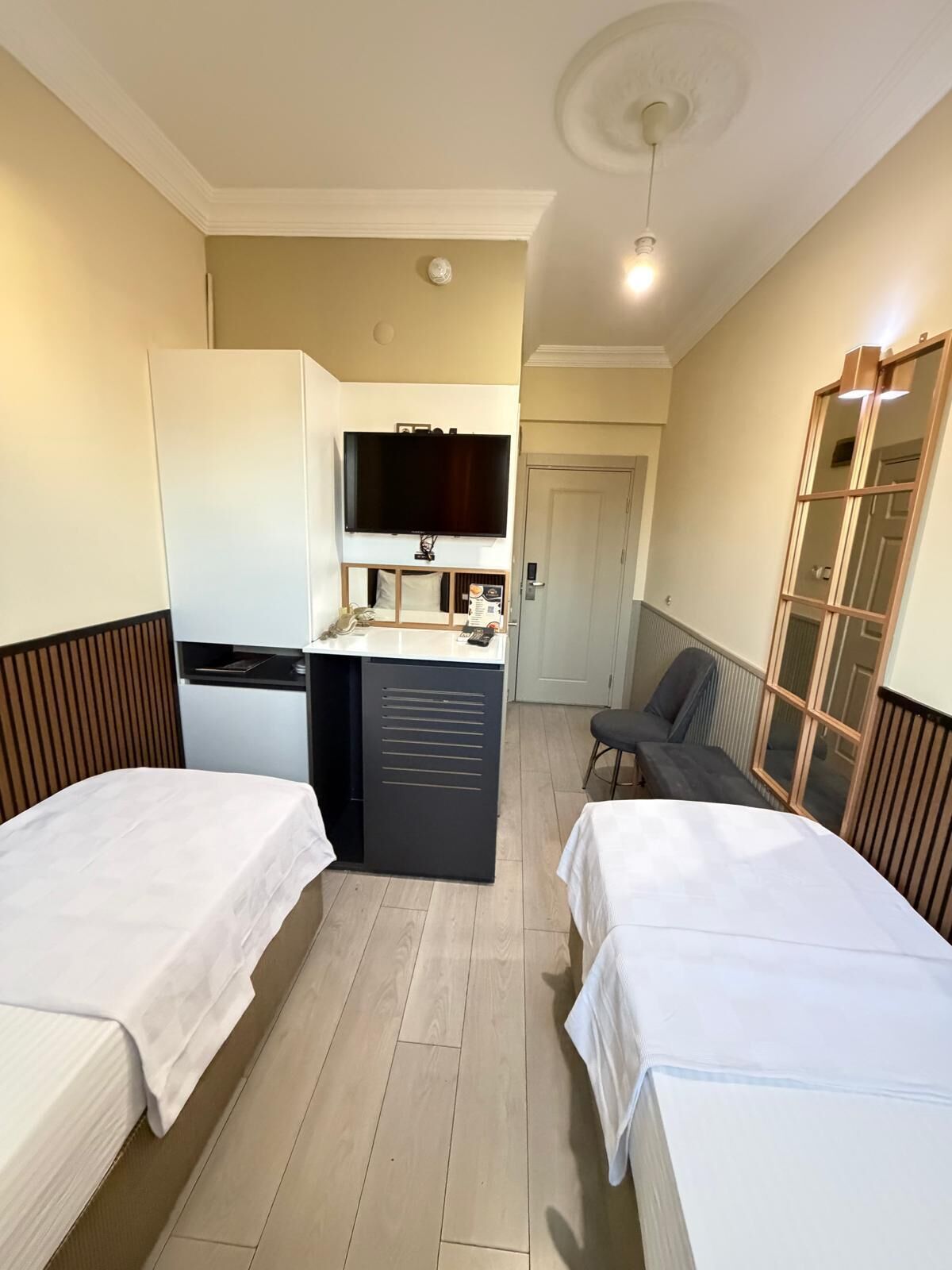 A compact hotel room with two single beds, a kitchenette, a TV, and a small seating area.