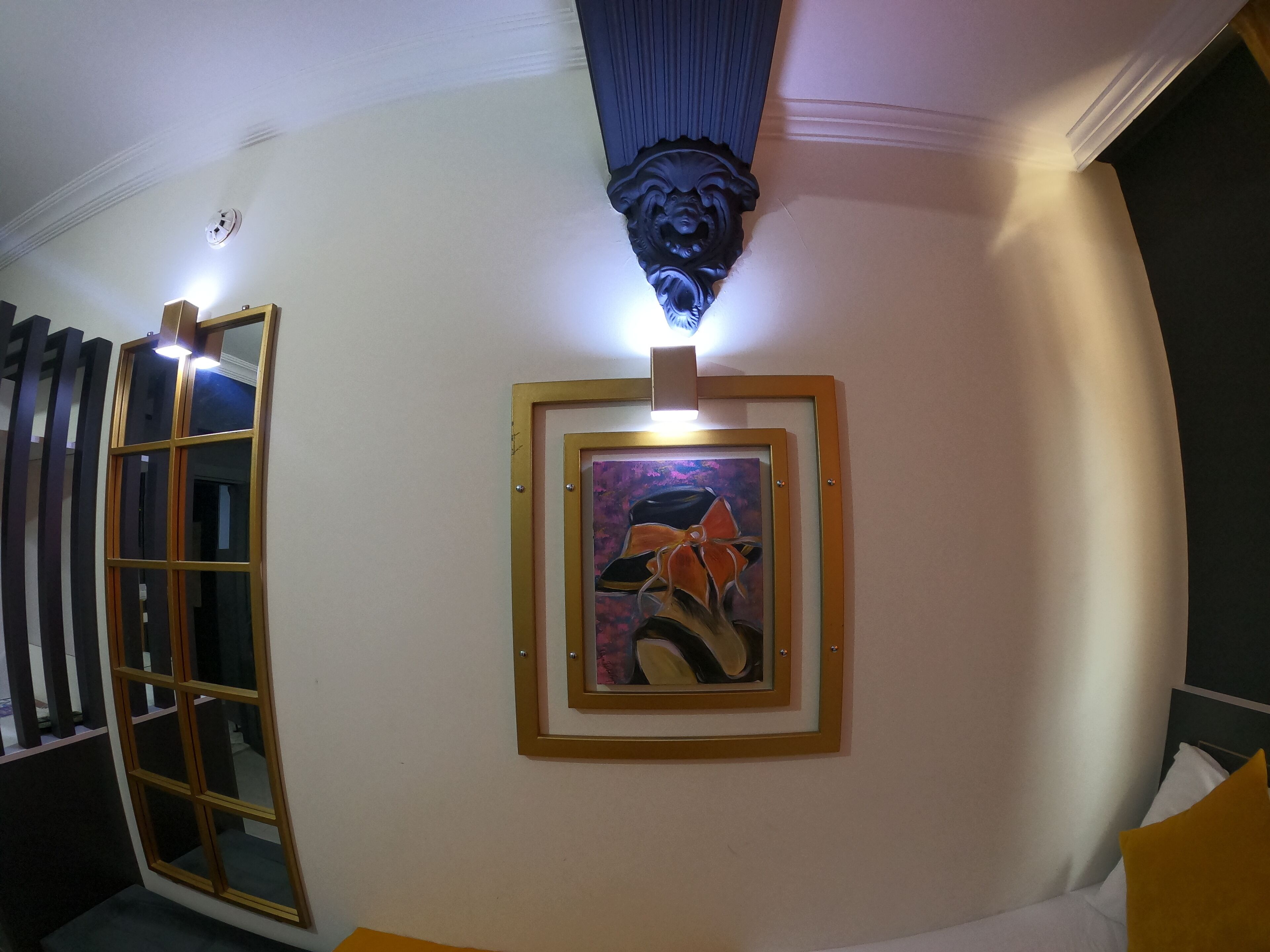 A room with a framed painting, a window with blinds, and a decorative ceiling element.