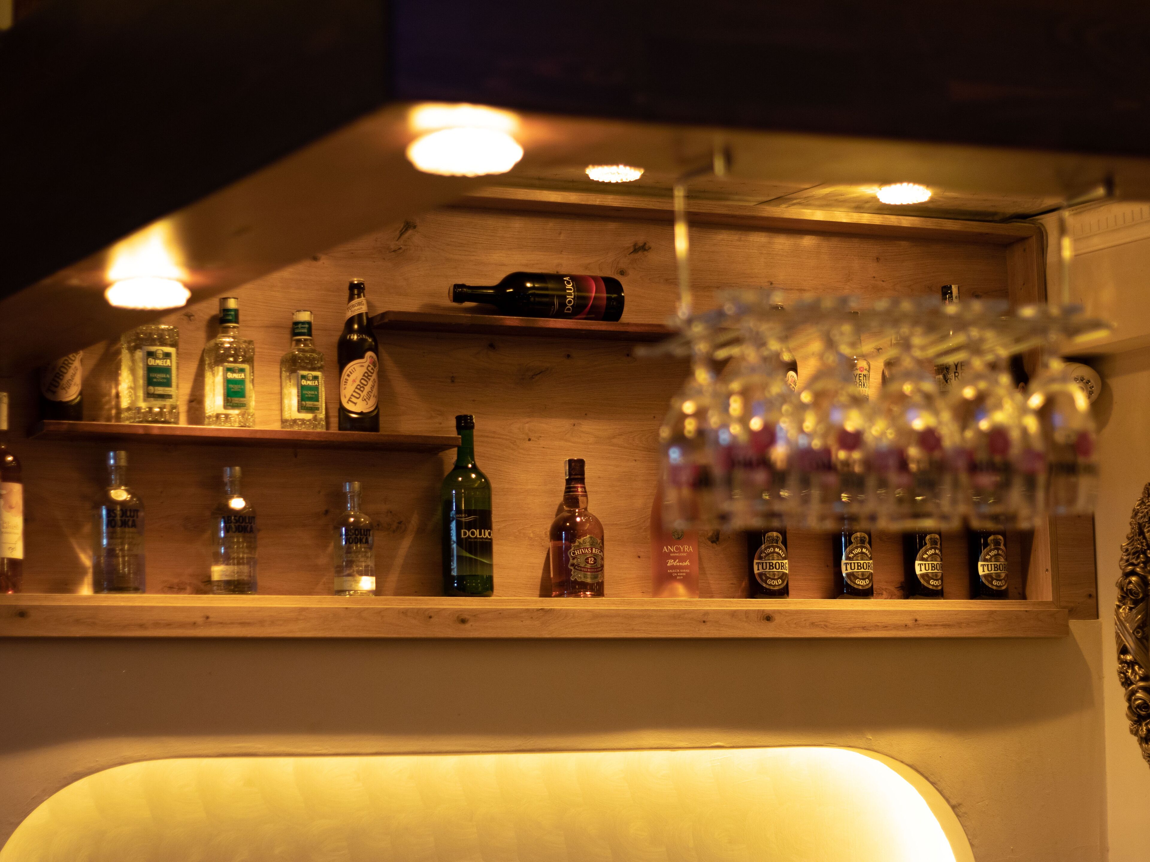 Zona de bar con estantes llenos de botellas de licor y un colgador para copas.