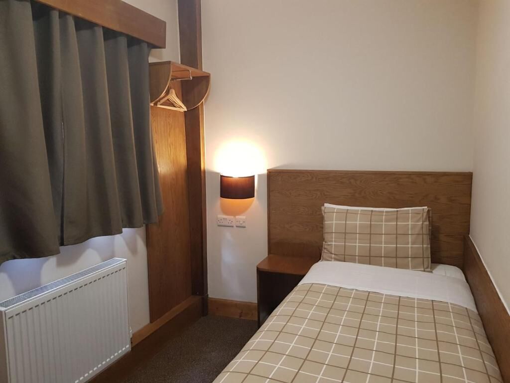 Et hotelværelse med seng, natbord, lampe, radiator og et træskab.