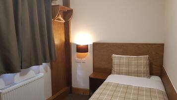 Et hotelværelse med seng, natbord, lampe, radiator og et træskab.