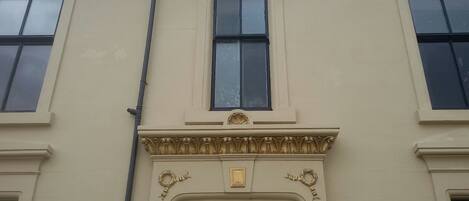 A building facade with three windows, a central entrance with decorative moldings, and a small plaque above the door.