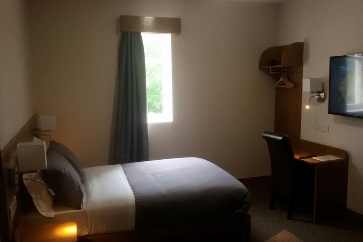 A hotel room with a bed, desk, chair, and a TV mounted on the wall.