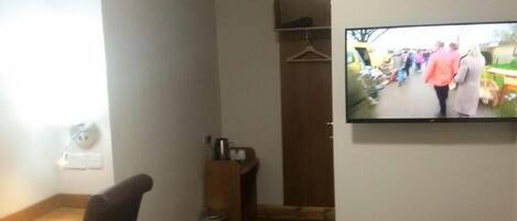 A hotel room with a desk, chair, TV, and a small closet.