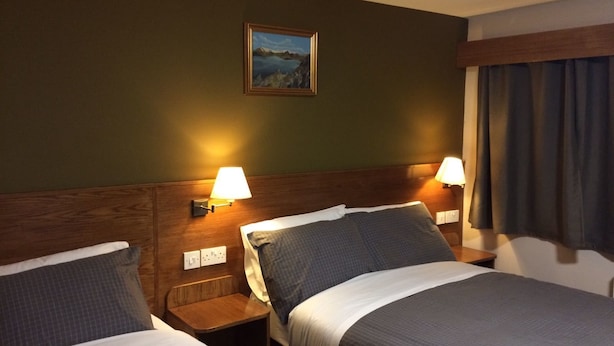 A hotel room with two beds, wooden headboards, and wall-mounted lamps. - Crosshill House (Glasgow)