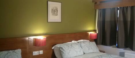 A hotel room with two beds, a headboard, bedside lamps, a framed picture on the wall, and a window with curtains.