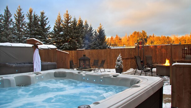 A hot tub surrounded by wooden deck and chairs, with a snowy landscape and trees in the background. - Auberge Motel Drakkar (Shawinigan)